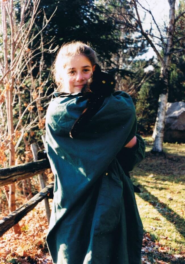 A young girl holds a black cat and smiles outside on a sunny autumn day.