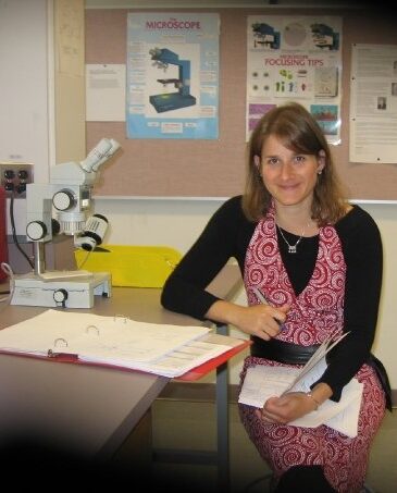 A woman academic studies calculations next to a microscope in a biology lab.