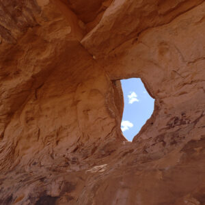 A window in a red sandstone cliff shows a blue sky on the other side.